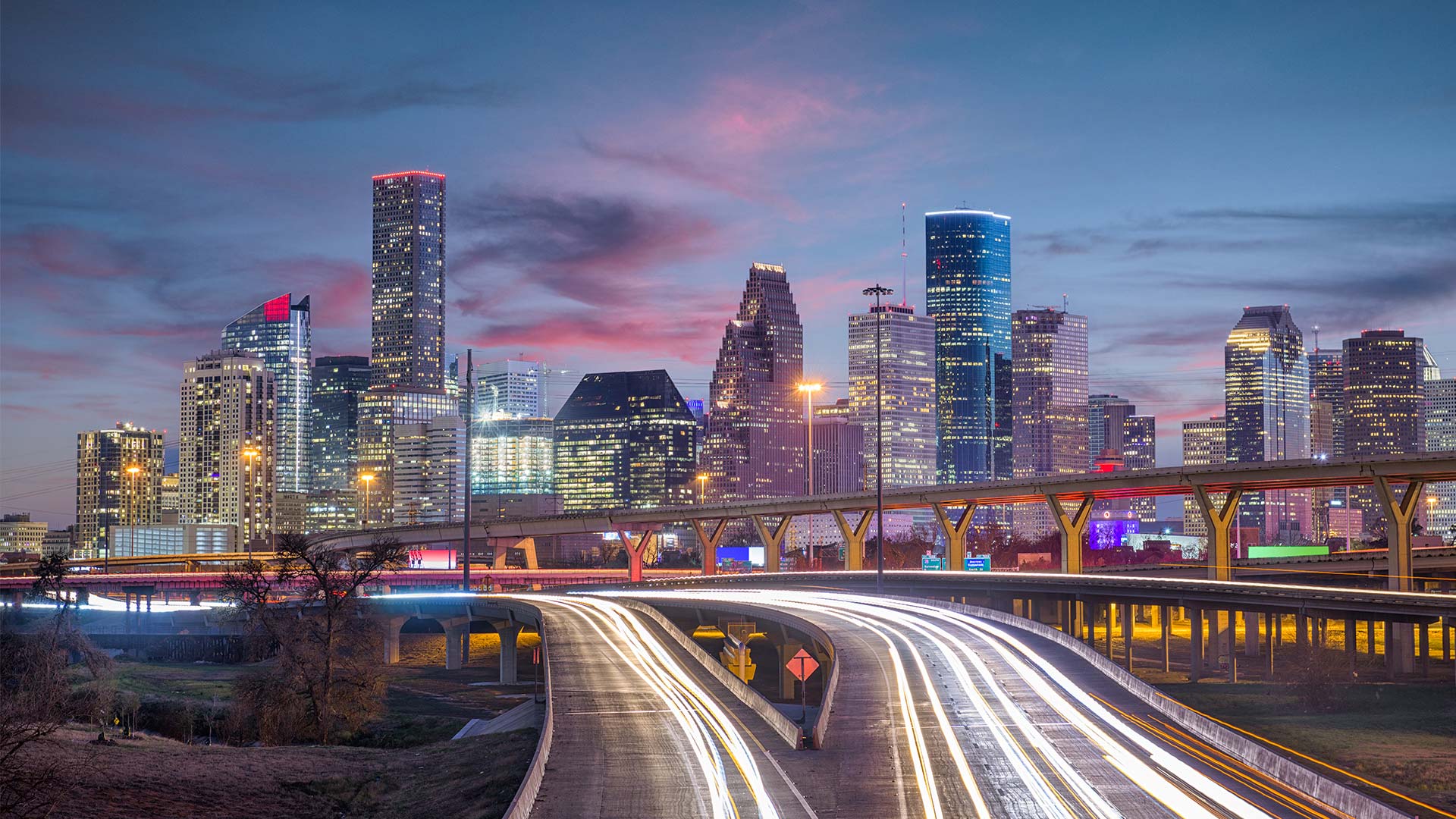Houston skyline at dusk with city lights and elevated train tracks.